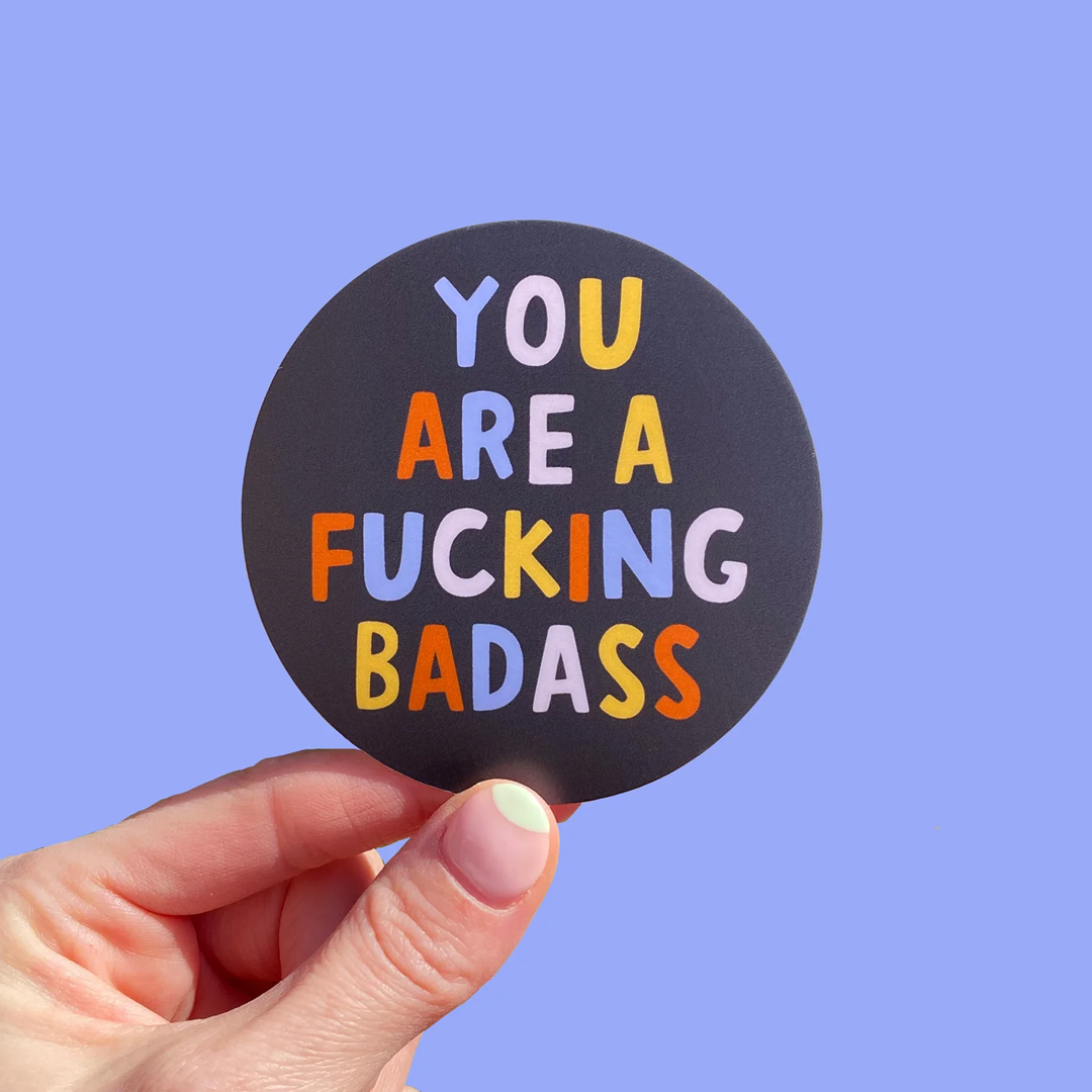 Black circular gloss vinylsticker with multicoloured text saying: "You are a fucking badass" on a purple background