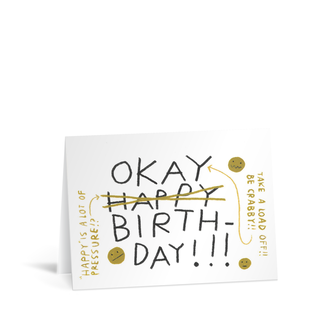 A card with quirky handwritten words saying "Happy Birthday" but the Happy has been crossed out an the word replaced with "OKAY" and a side note saying "Happy is a lot of pressure" and on the other side another note saying "take a load off - be crabby"