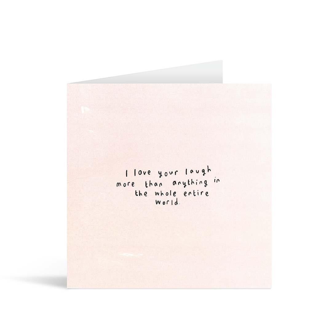 A textured pale pink card with the handwritten words "I love your laugh more than anything in the whole entire world"