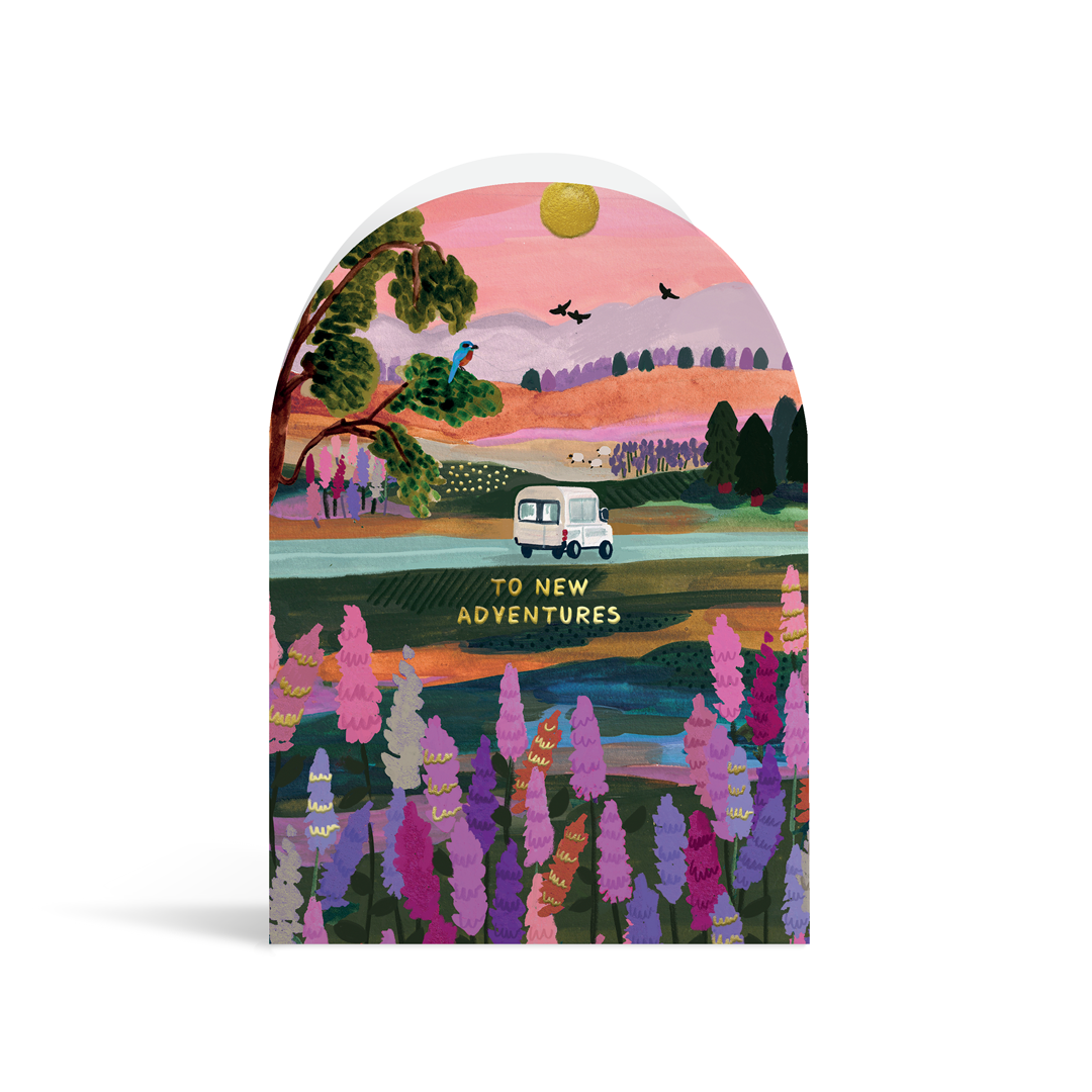 A bright, arch shaped card painted vibrant pinks, purples and greens with gold foil highlights. In the centre of the picturesque image is a white camper van dribving away above the gold foiled text "to new adventures"