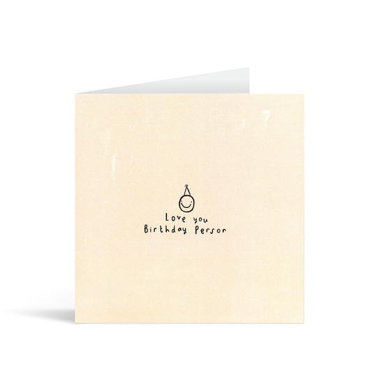 A textured cream card with a cute and cheeky illustration of a smiling face in a party hat and handwritten words "Love you birthday person"