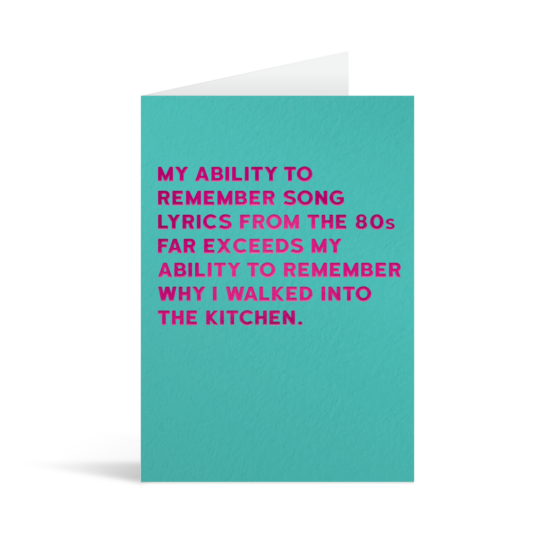 Turquoise rectangular card with fuschia foiled text saying: " My ability to remember song lyrics from the 80'sfar exceeds my ability to remember why I walked into the kitchen." , with white envelope in the background.