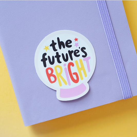 White crystal ball gloss vinyl sticker with multicoloured text saying: "The future's bright" on a lilac notebook.