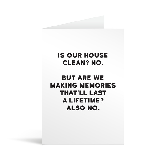 White rectangular card with black text saying: "Is our house clean? No. But are we making memories that'll last a lifetime? Also no."