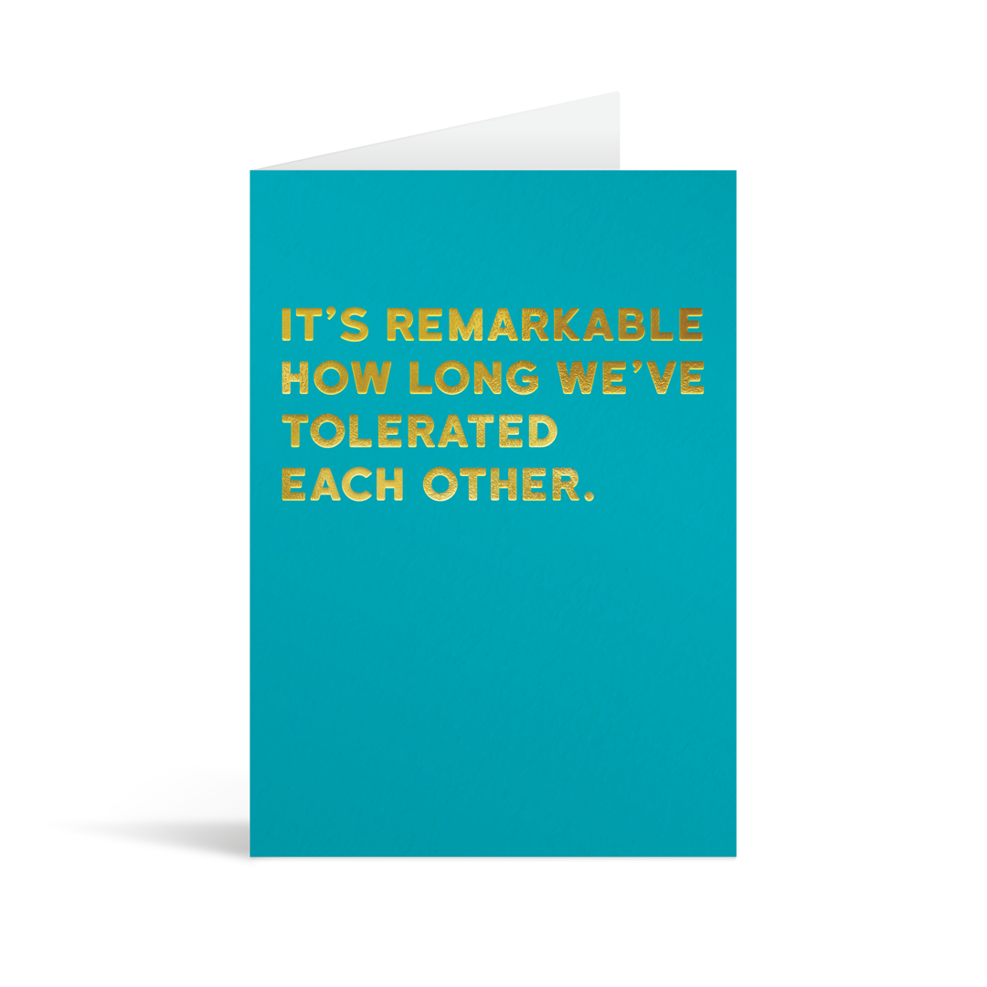 Bright blue rectangular card with gold foiled text saying: "It's remarkable how long we've tolerated each other." 