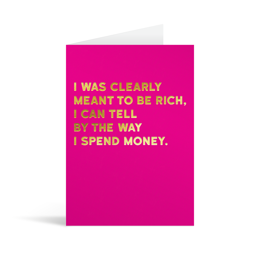 Bright pink rectangular card with gold foiled text saying: "I was clearly meant to be rich, I can tell by the way I spend money"