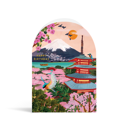 A bright, arch-shaped card painted in vibrant turquoises, greens, pinks and peach tones. The scene depicts Mount Fuji with a typical Japanese style building and bright blue bird in the foreground, and gold foiled text reading Happy Birthday