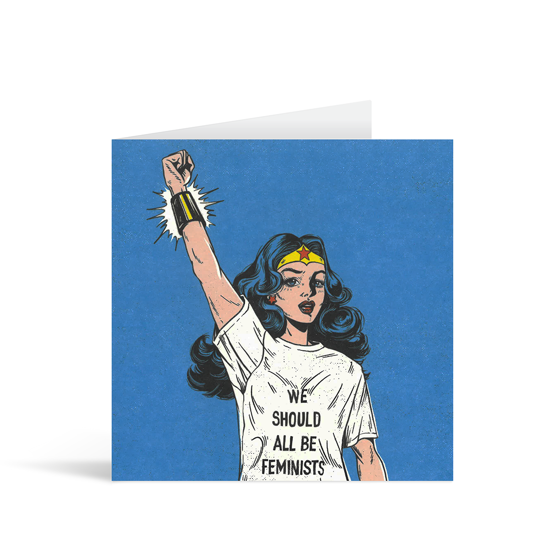 A square blue card with a stylised image of a woman who resembles Wonder Woman, wearing a t shirt which reads "We should all be feminists"