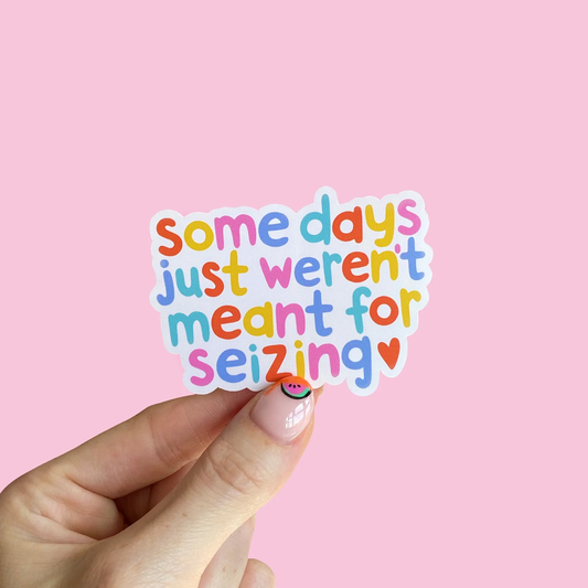 White gloss vinyl sticker with multicoloured text saying: "Some days just weren't meant for seizing" on a pastel pink background.