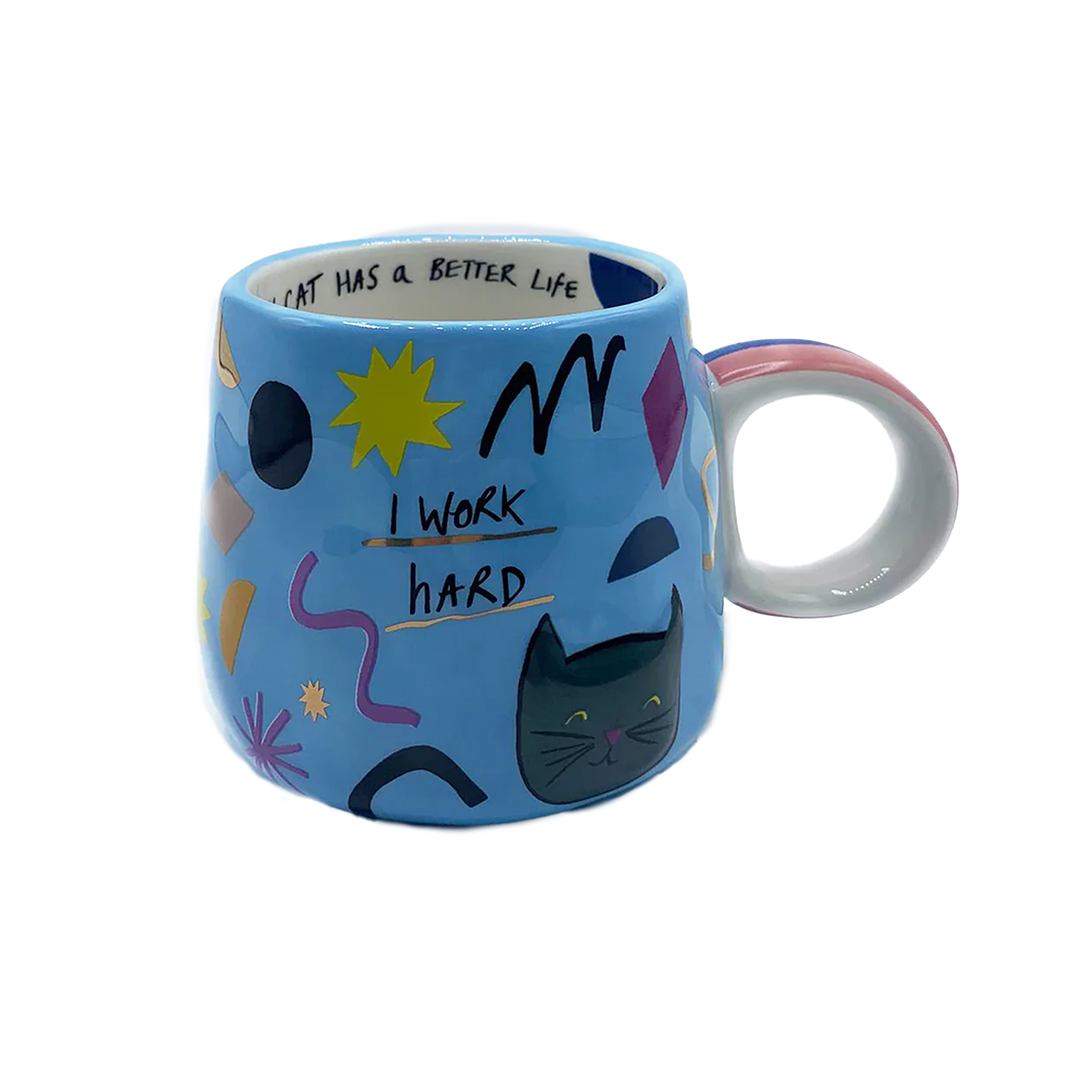 Front facing blue mug with abstract shapes and a cat surrounding black text saying "I work hard" underlined with gold metallic paint