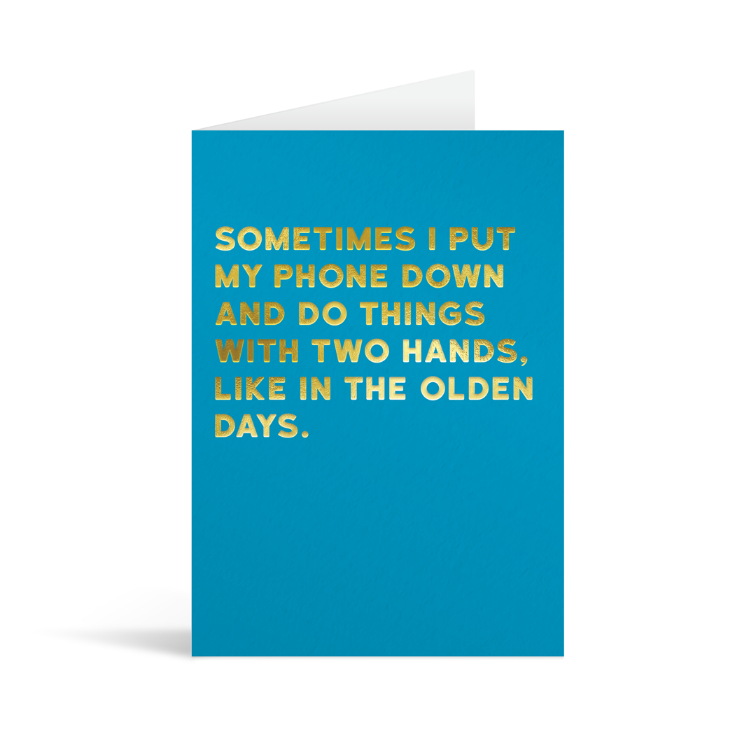 Bright blue rectangular card with gold foiled text reading "Sometimes I put my phone down and do things with two hands like in the olden days".