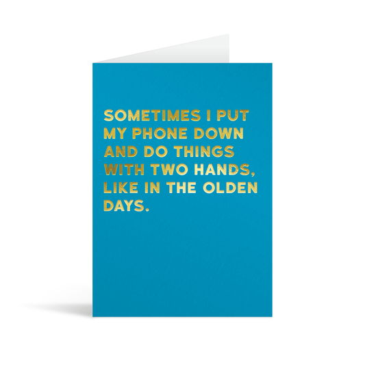 Bright blue rectangular card with gold foiled text reading "Sometimes I put my phone down and do things with two hands like in the olden days".