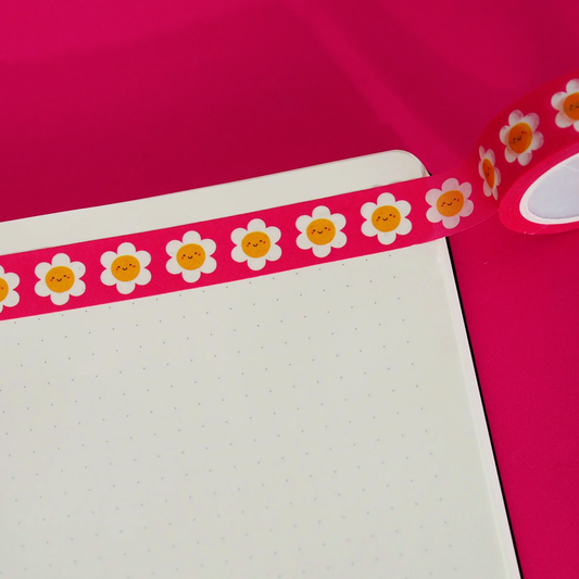 A strip of cute red washi tape  daisies with smiley faces stuck onto a sheet of dotted paper on a red background