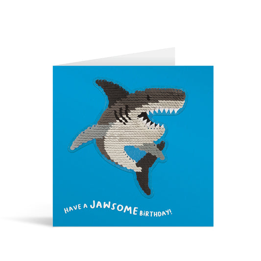 Blue square greetings card with reversible sequin shark patch and fun, free-flowing text that reads "Have a JAWSOME Birthday!"
