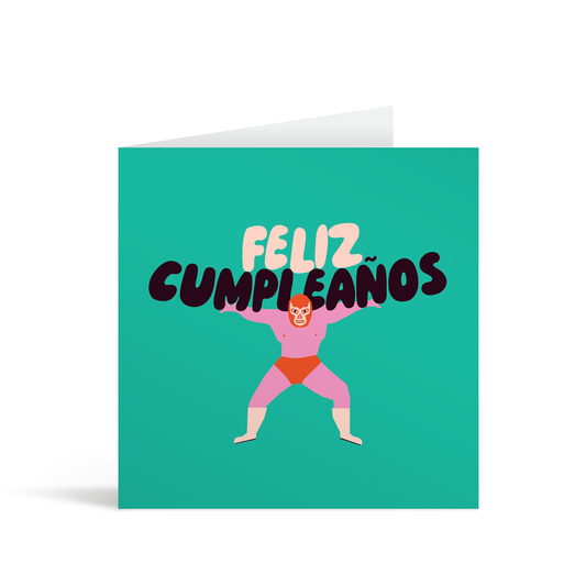 A turquoise square card with a cartoon style wrestler in pink and red lycra, holding on his shoulders the words "Feliz Cumpleanos". Brown envelope in background.