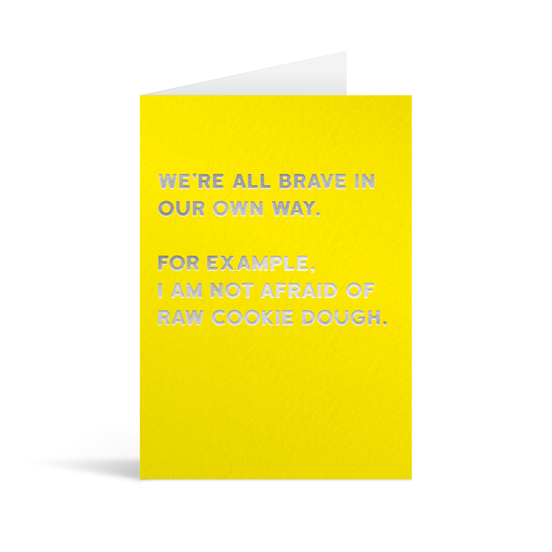 Bright yellow rectangular card with silver foiled text reading "We're all brave in our own way. For example I am not afraid of cookie dough".