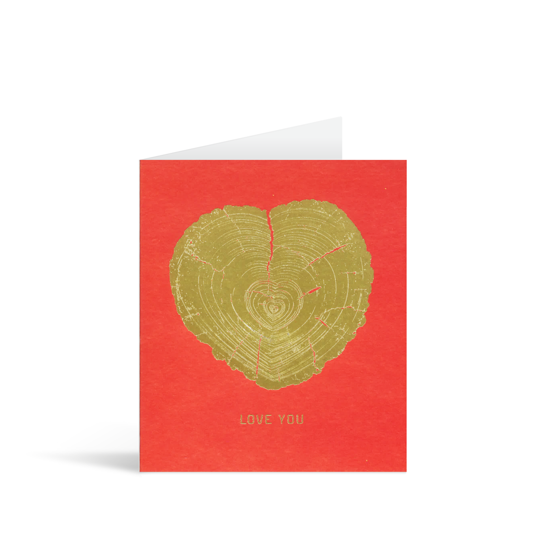 A valentine's red card with a gold foiled block print of heartshaped tree rings above the words LOVE YOU.