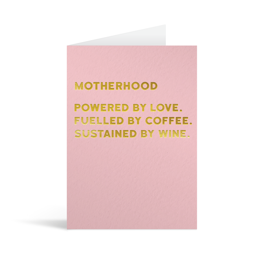 Pink rectangular card with funny gold foiled text saying "Motherhood powered by love. Fuelled by coffee. Sustained by wine."