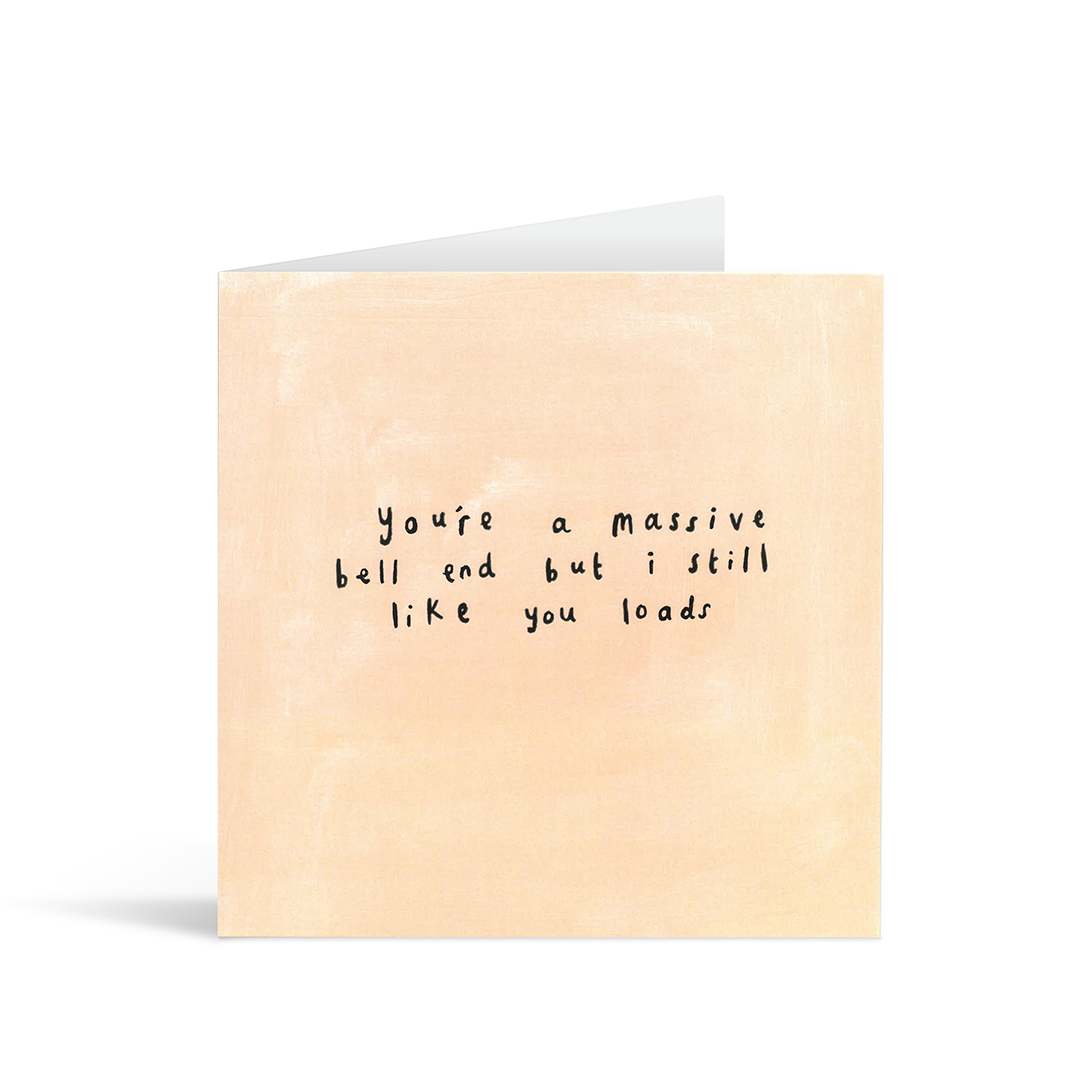 A textured pale orange card with the handwritten words "You're a massive bell end but I still like you lots"