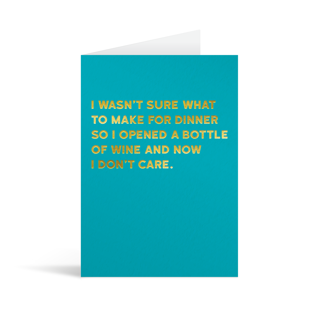 Blue rectangular card with gold foiled text saying "I wasn't sure what to make for dinner so I opened a bottle of wine and now I don't care." 