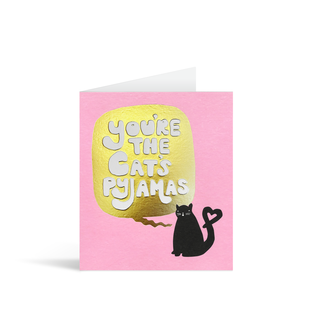 A bubblegum pink card with a block print of a quirky cat, complete with heart shaped kink in its tail, and the writing  on a gold foiled speech bubble which reads "You're the cat's pyjamas"