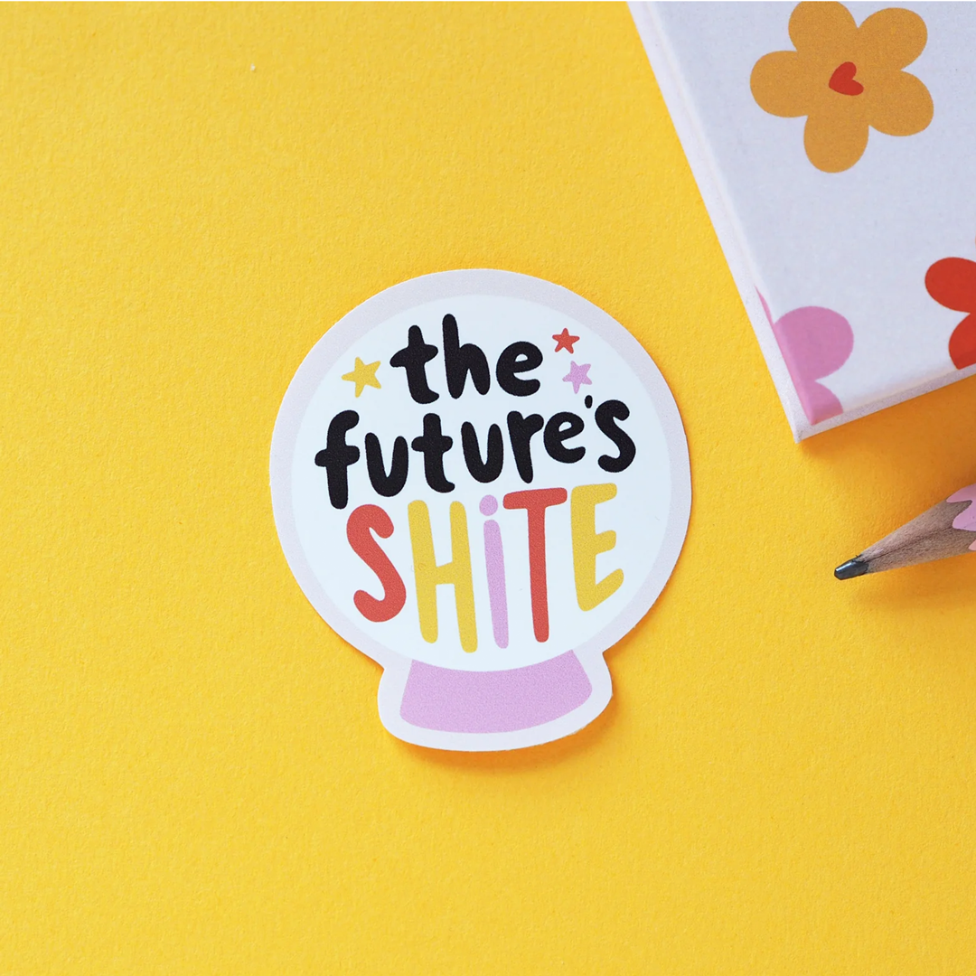 White crystal ball gloss vinyl sticker with multicoloured text saying: "The future's shite" on a lilac notebook.