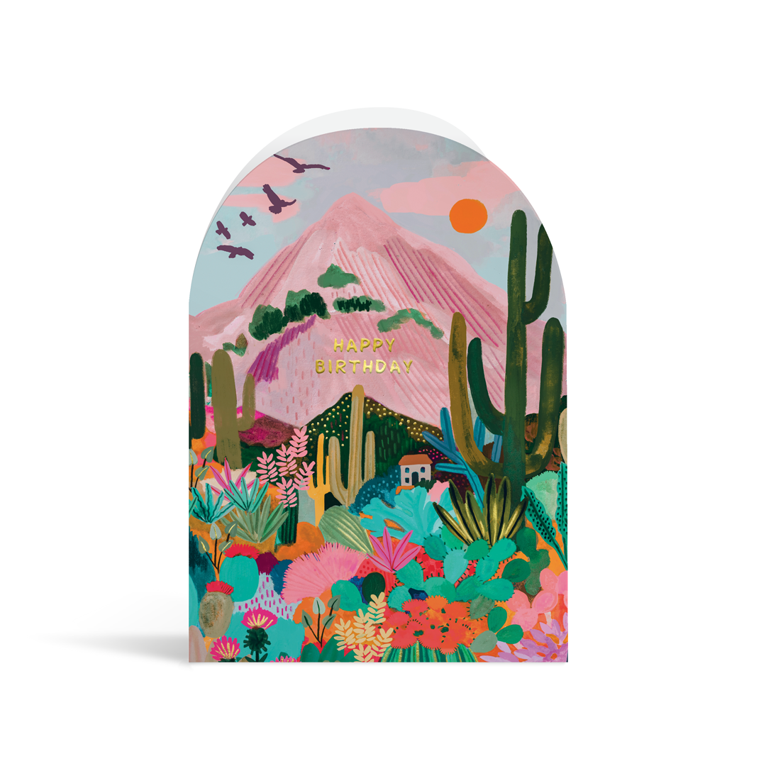 A bright, arch-shaped card painted in vibrant turquoises, greens, pinks and peach tones. The scene depicts a mountain in the background with bold succulents and cacti in the foreground, and gold foiled text reading Happy Birthday