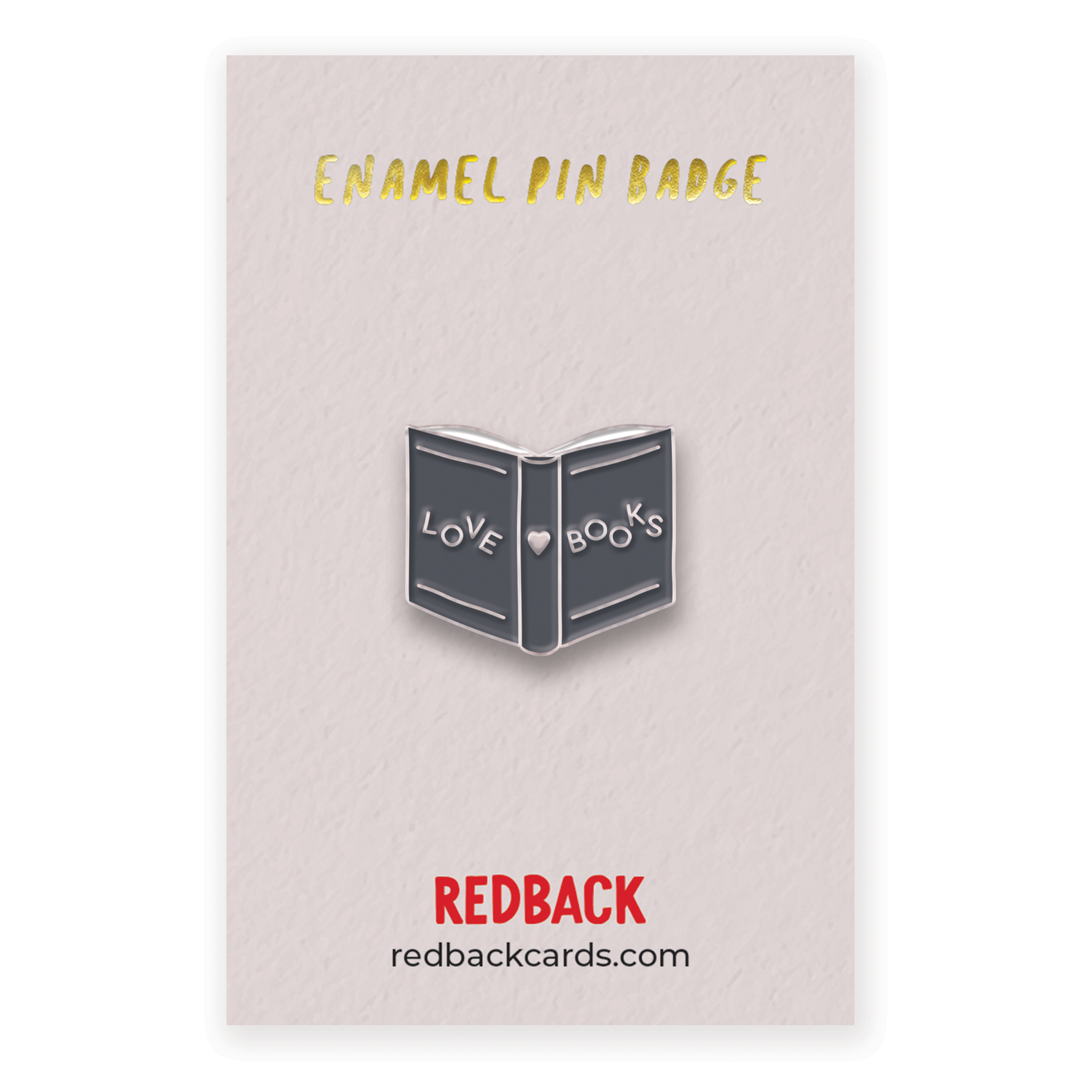 A cute black book enamel pin with silver text across the cover saying love books. Mounted on card.