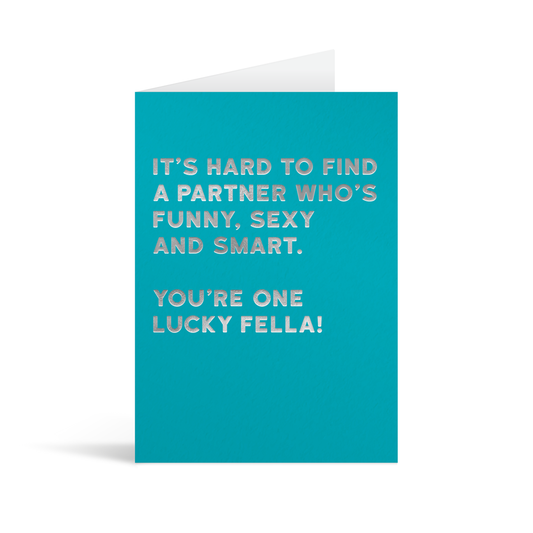 Bright blue rectangular card with funny silver foiled text saying "It's hard to find a partner who's funny, sexy and smart. You're one lucky fella!"